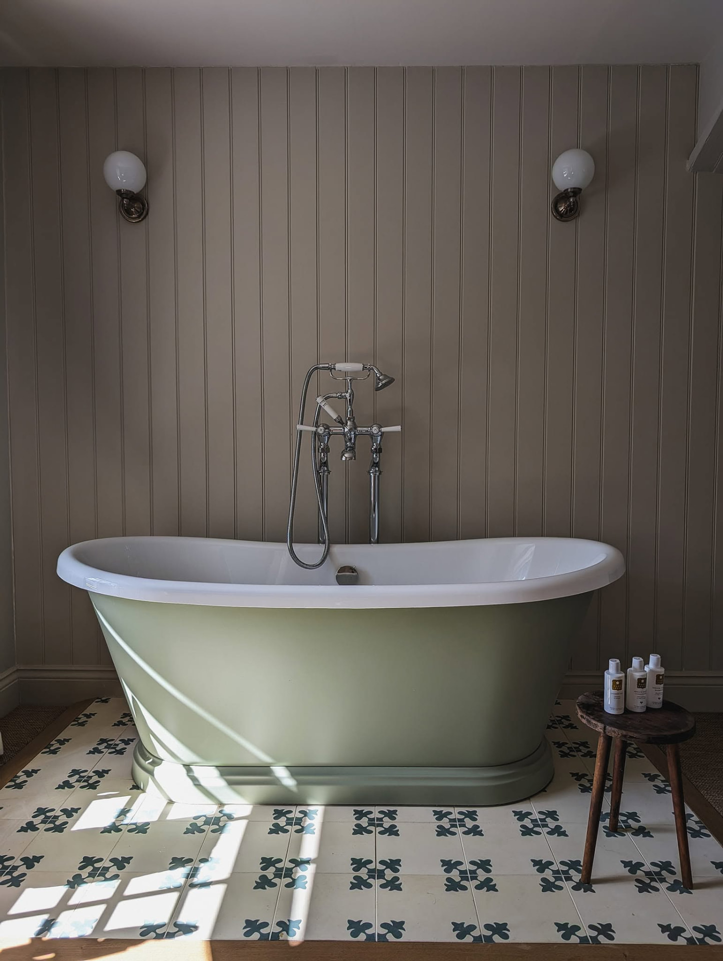 Panelled bathroom with sage green freestanding bath and patterned tiled floor